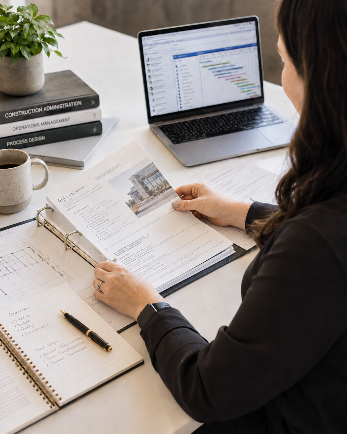 AEC firm owner reviewing project documents at desk with construction administration books, architectural drawings, and project management software open on laptop